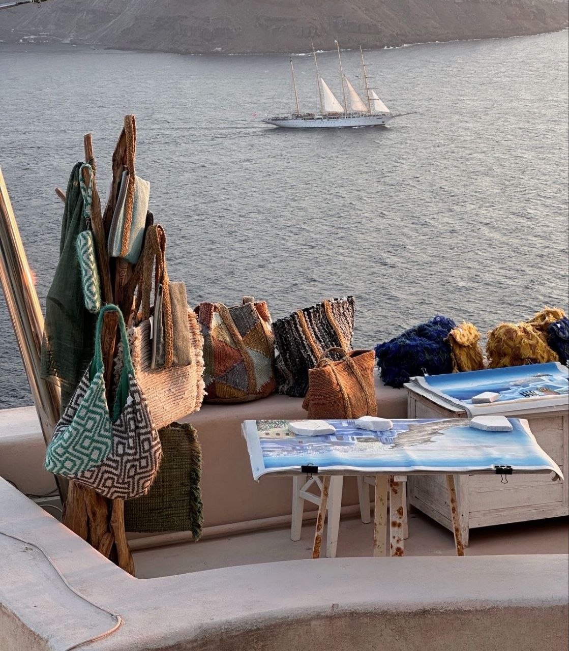 Artisan craft display on Santorini terrace with a three-masted sailing ship in the background