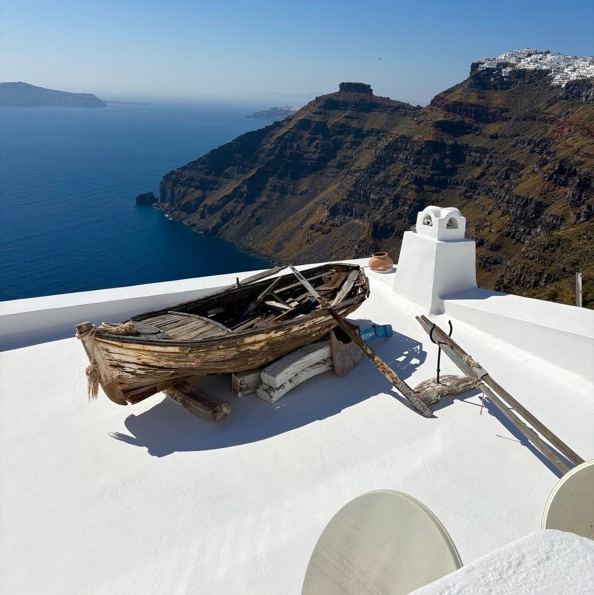 Traditional weathered fishing boat on whitewashed Santorini terrace with caldera cliffs in the background